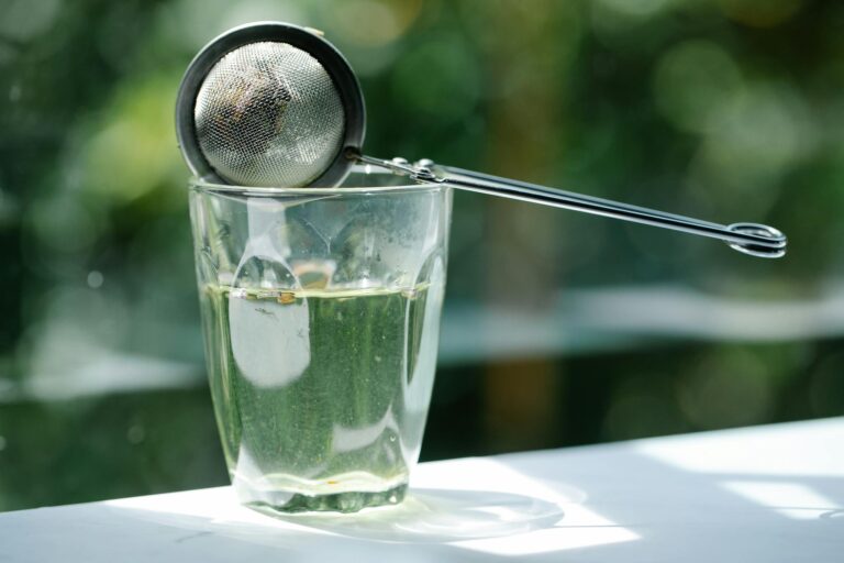 Close-up of glass with tea infuser in sunlight, highlighting serenity and refreshment.