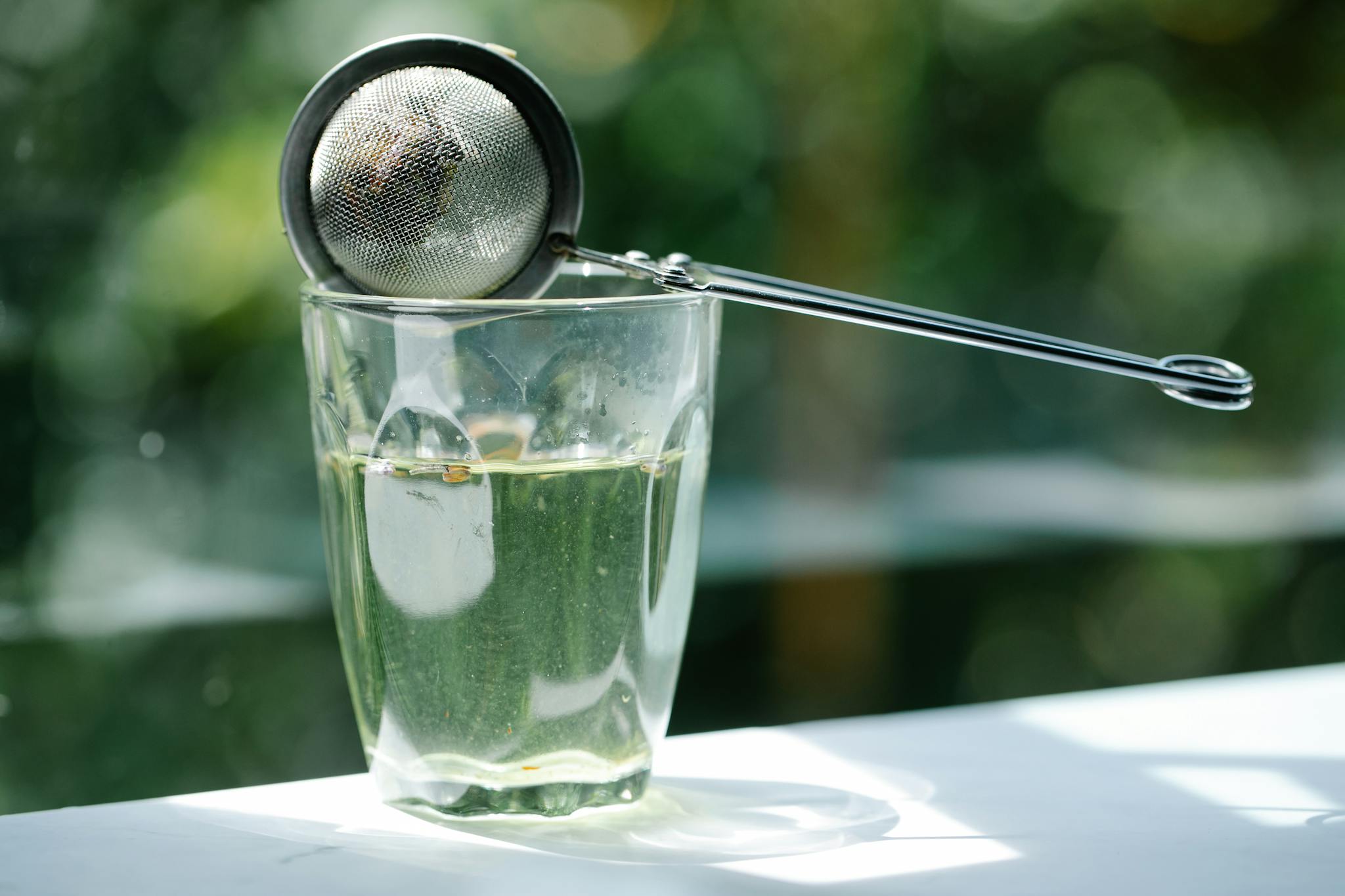 Close-up of glass with tea infuser in sunlight, highlighting serenity and refreshment.